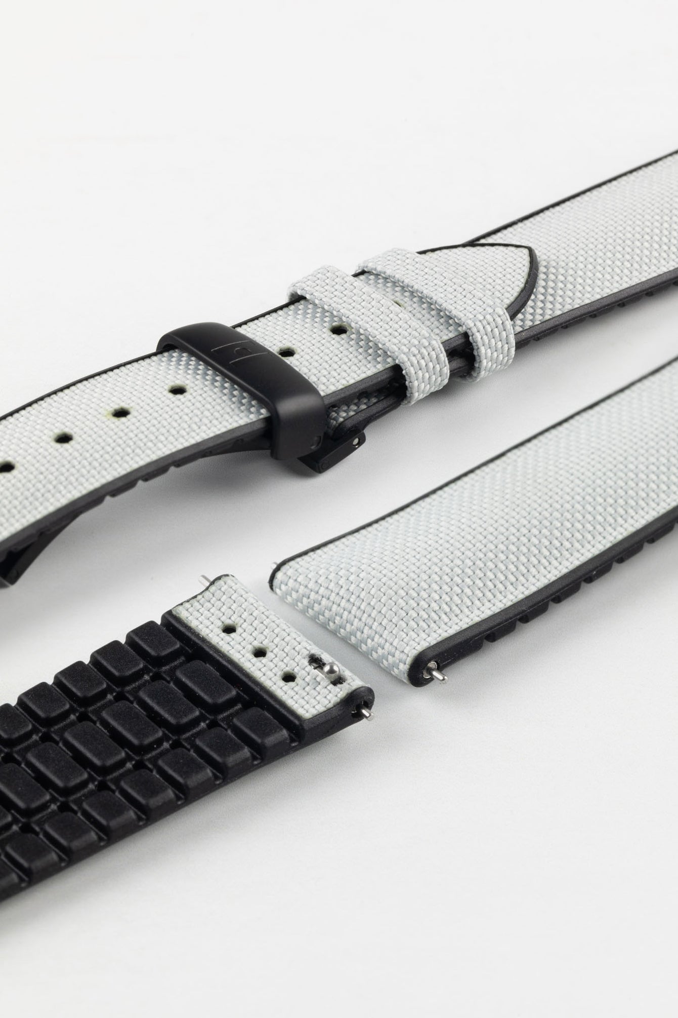 A detailed, slightly angled shot of a light grey Hirsch Arne Performance Watch Strap, laid in two pieces on a white background, highlighting its woven grey upper, black ribbed underside, and a black deployment clasp.