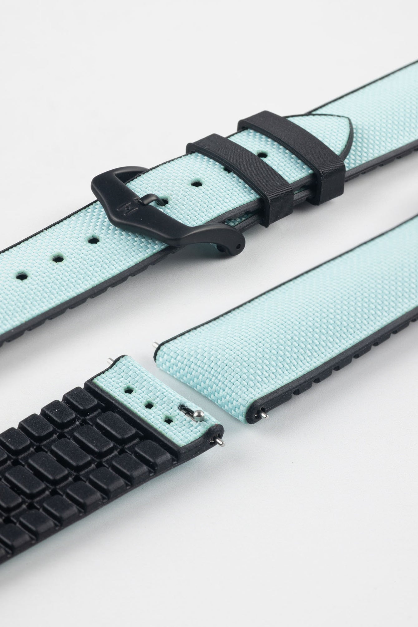 Ice blue textile-effect watch strap with black rubber backing and a black buckle, shown in separate sections on a white background. Features a woven-look surface, black edges, and a patterned rubber underside.
