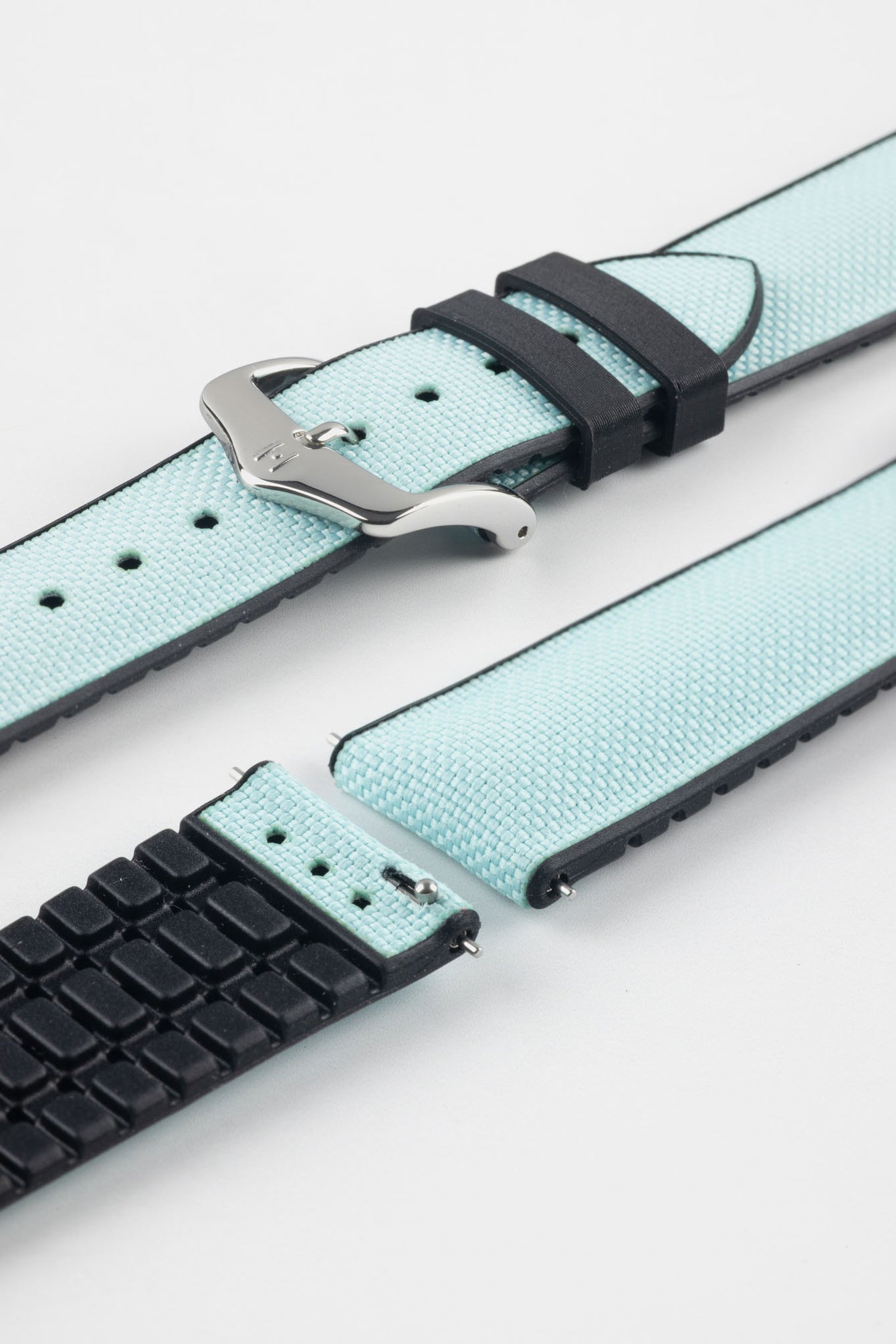 Ice blue textile-effect watch strap with black rubber backing and a silver-tone buckle, shown in separate sections on a white background. Features a woven-look surface, black edges, and a patterned rubber underside.