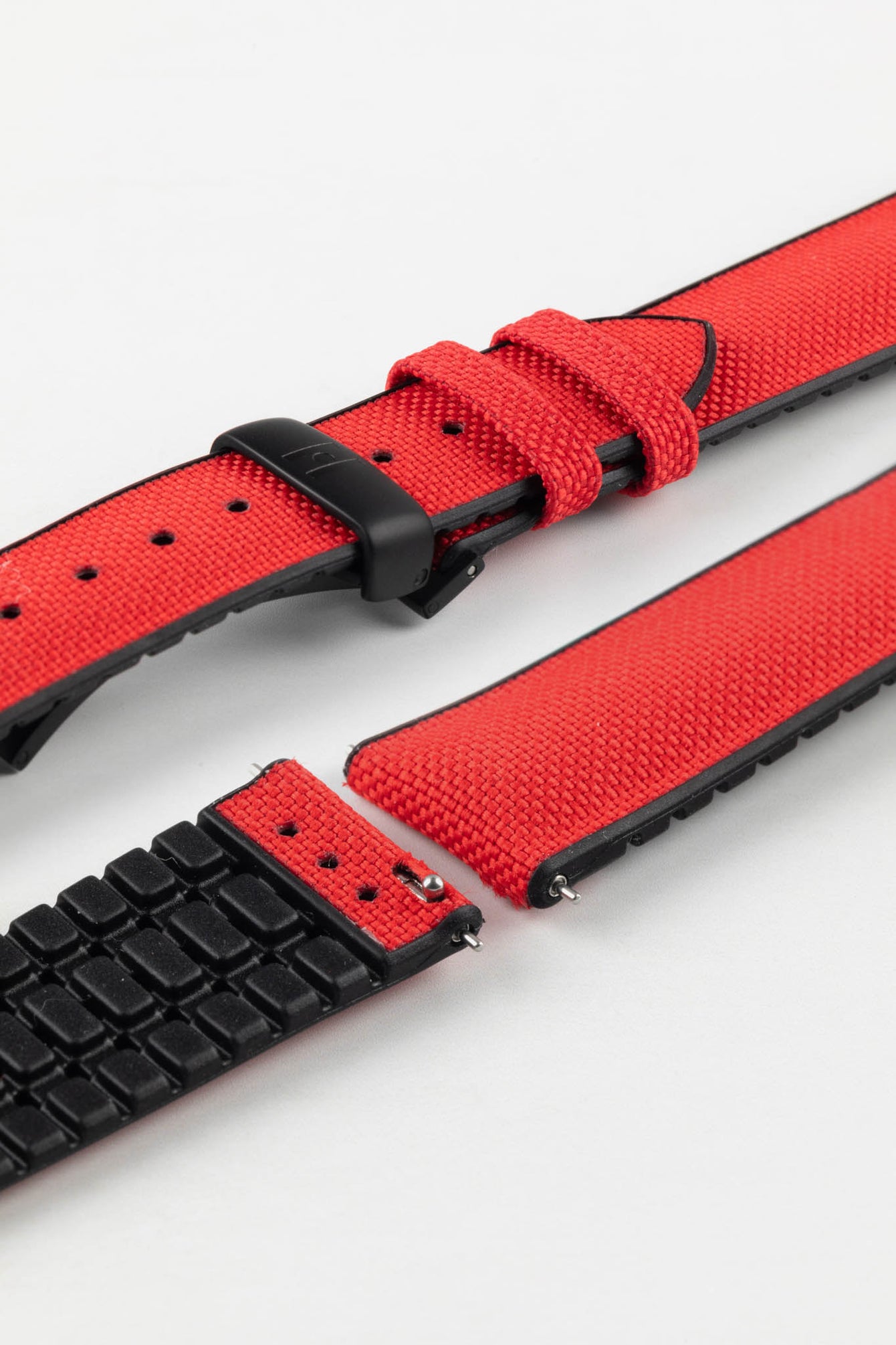 A detailed, slightly angled shot of a red Hirsch Arne Performance Watch Strap, laid in two pieces on a white background, highlighting its woven red upper, black ribbed underside, and a black deployment clasp.