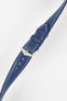 Close-up of a blue textured leather watch strap with white contrast stitching, featuring a polished silver-tone pin buckle and two keepers, with visible adjustment holes and a lightly grained finish against a white background.