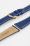 Close-up product image of a blue textured leather watch strap with white contrast stitching, displayed against a white background, featuring a polished gold-tone pin buckle and two keepers, alongside separate strap sections with exposed spring bars and a beige underside stamped with partial text “20 HIRSCH Bologna.”