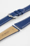 Close-up product image of a blue textured leather watch strap with white contrast stitching, displayed against a white background, featuring a polished silver-tone pin buckle and two keepers, alongside separate strap sections with exposed spring bars and a beige underside stamped with partial text “20 HIRSCH Bologna.”
