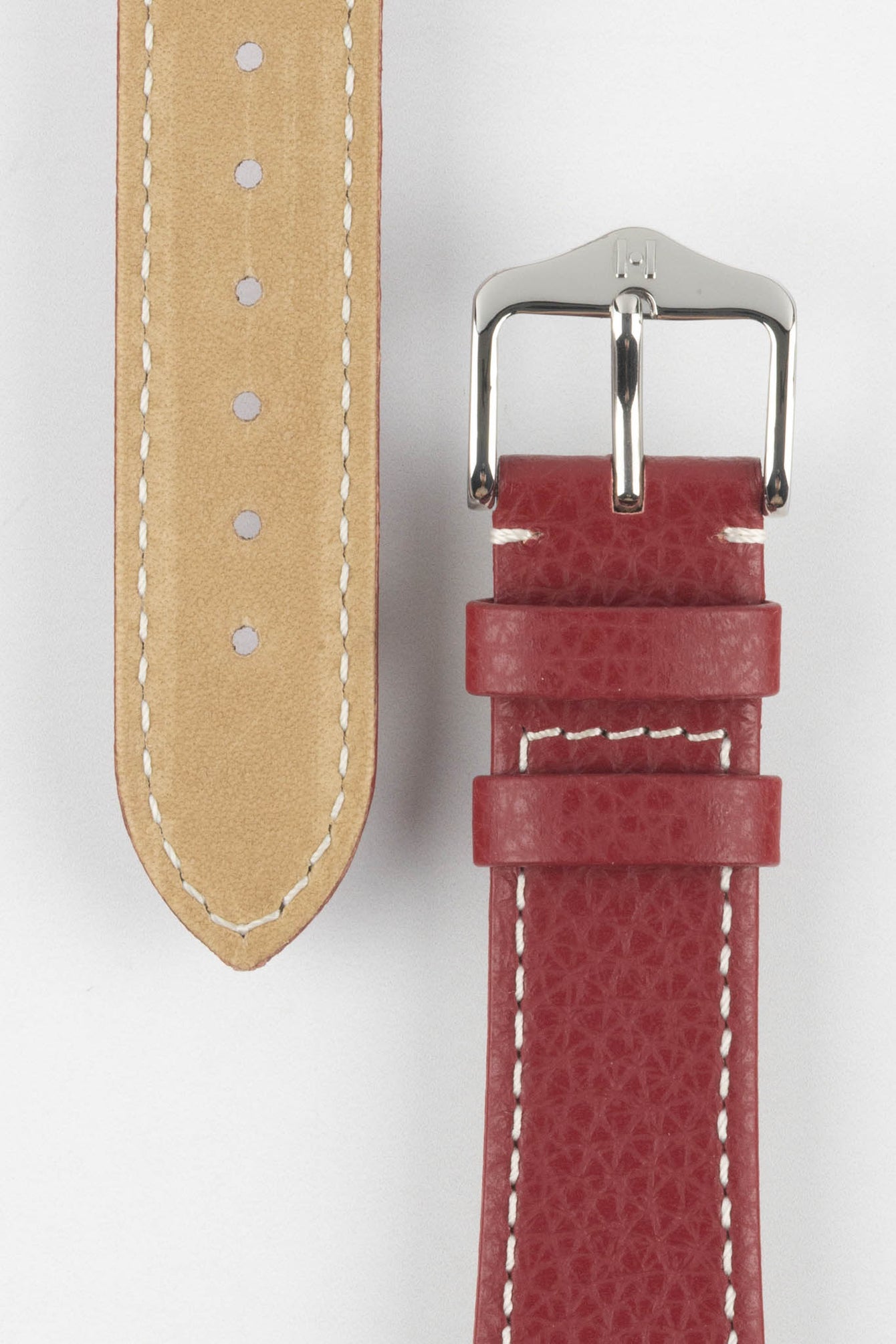 Close-up product image of a red textured leather watch strap on a white background, showing the underside with multiple adjustment holes and beige lining on one section, and the other with a polished silver-tone pin buckle and two keepers, highlighting the white contrast stitching and fine grain pattern.