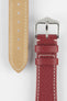 Close-up product image of a red textured leather watch strap on a white background, showing the underside with multiple adjustment holes and beige lining on one section, and the other with a polished silver-tone pin buckle and two keepers, highlighting the white contrast stitching and fine grain pattern.