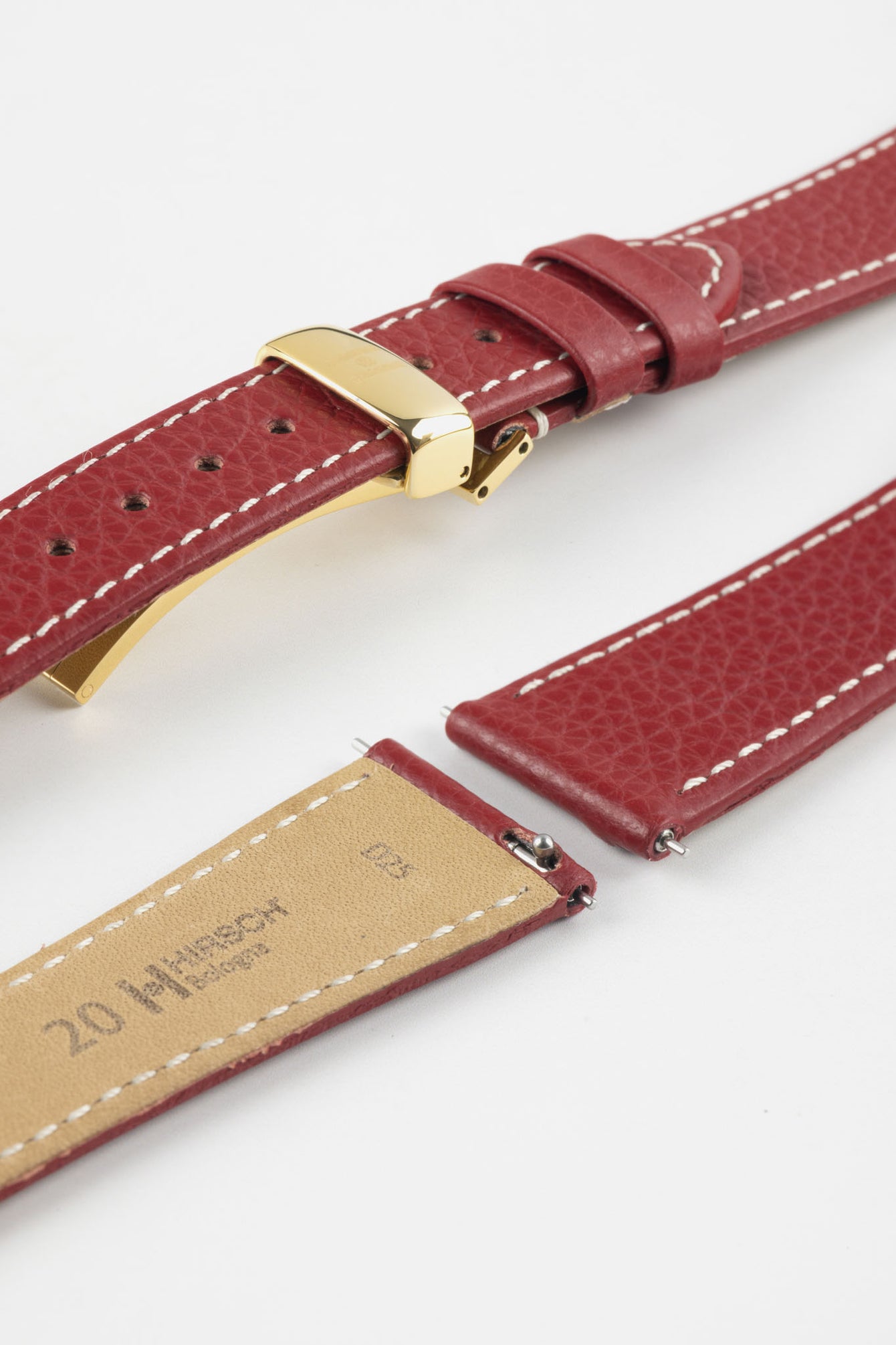 Close-up product image of a red textured leather watch strap with white contrast stitching, shown against a white background, featuring a polished gold-tone folding clasp and two keepers, alongside separate strap sections with visible spring bars and a beige underside stamped with partial text “20 HIRSCH.”