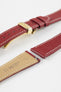 Close-up product image of a red textured leather watch strap with white contrast stitching, shown against a white background, featuring a polished gold-tone folding clasp and two keepers, alongside separate strap sections with visible spring bars and a beige underside stamped with partial text “20 HIRSCH.”