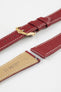 Close-up product image of a red textured leather watch strap with white contrast stitching, shown against a white background, featuring a polished gold-tone pin buckle and two keepers, alongside separate strap sections with visible spring bars and a beige underside stamped with partial text “20 HIRSCH.”