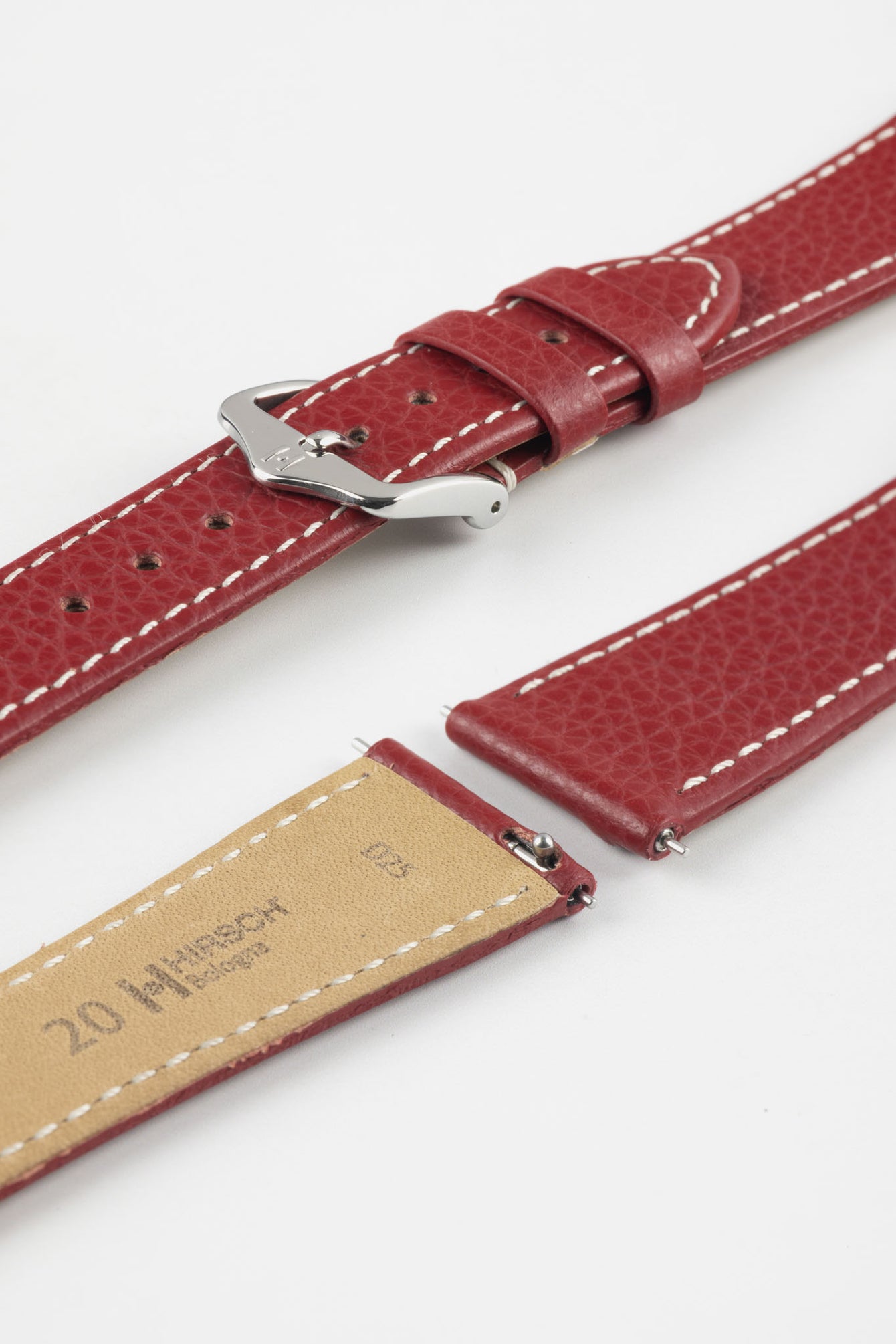 Close-up product image of a red textured leather watch strap with white contrast stitching, shown against a white background, featuring a polished silver-tone pin buckle and two keepers, alongside separate strap sections with visible spring bars and a beige underside stamped with partial branding text “20 HIRSCH.”