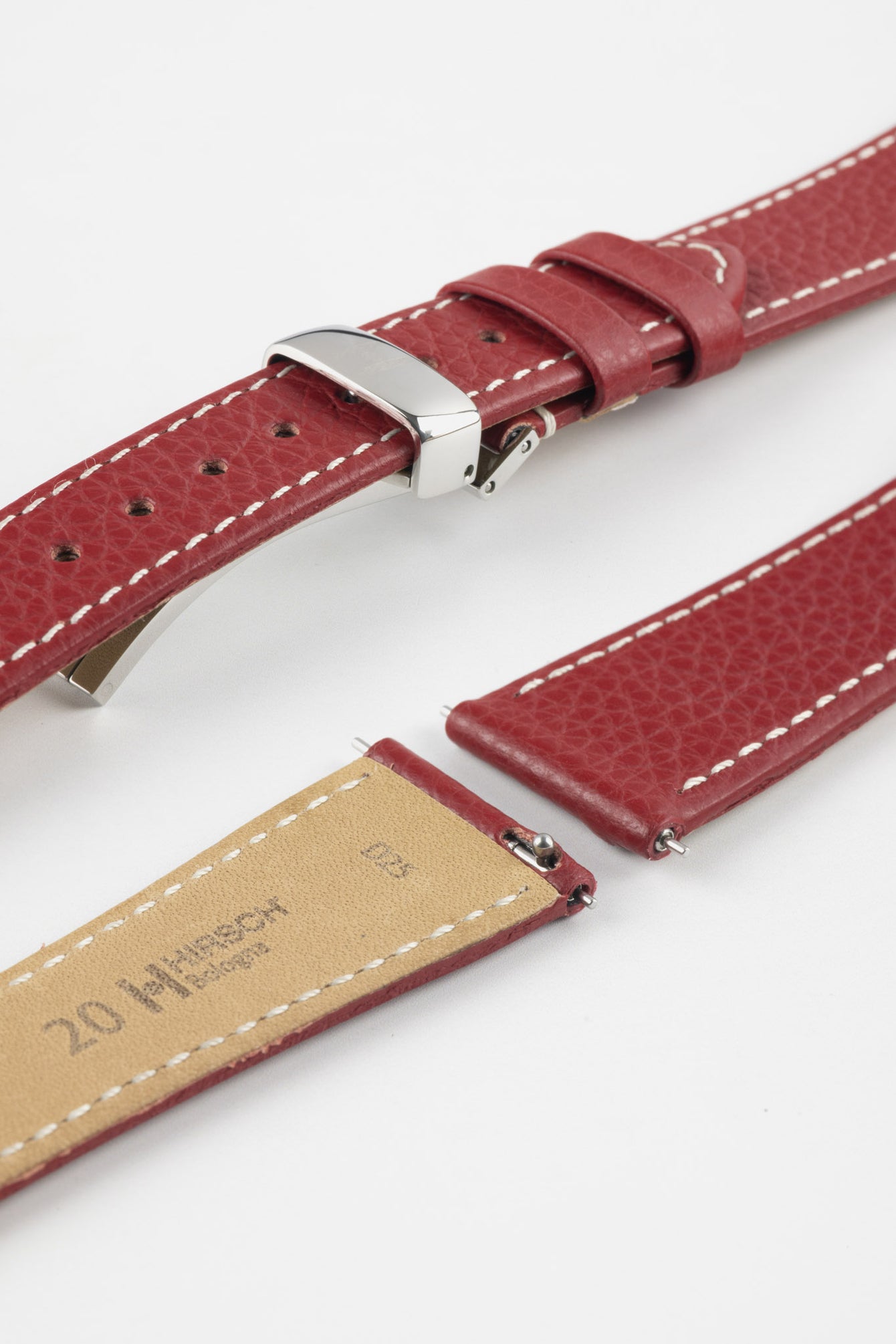 Close-up product image of a red textured leather watch strap with white contrast stitching, shown against a white background, featuring a polished silver-tone folding clasp and two keepers, alongside separate strap sections with visible spring bars and a beige underside stamped with partial text “20 HIRSCH.”