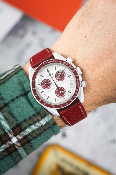 Omega x Swatch MoonSwatch with white dial and burgundy bezel on a matching leather strap, worn on a wrist.