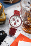 Omega x Swatch MoonSwatch with a white dial and burgundy bezel on a matching leather strap, styled beside a glass of whisky and accessories.