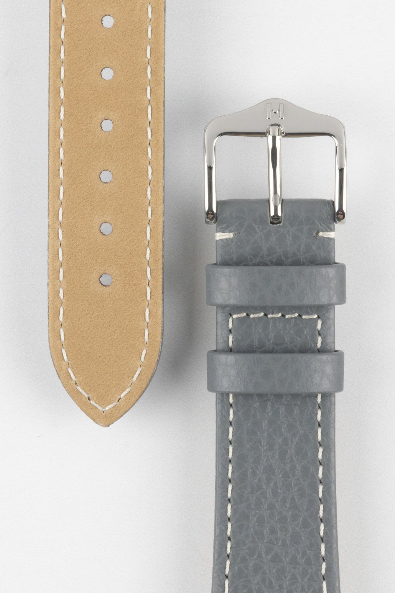 Close-up product image of a grey textured leather watch strap on a white background, showing the underside with multiple adjustment holes and beige lining on one section, and the other with a polished silver-tone pin buckle and two keepers, highlighting the white contrast stitching and fine grain pattern.
