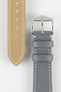 Close-up product image of a grey textured leather watch strap on a white background, showing the underside with multiple adjustment holes and beige lining on one section, and the other with a polished silver-tone pin buckle and two keepers, highlighting the white contrast stitching and fine grain pattern.