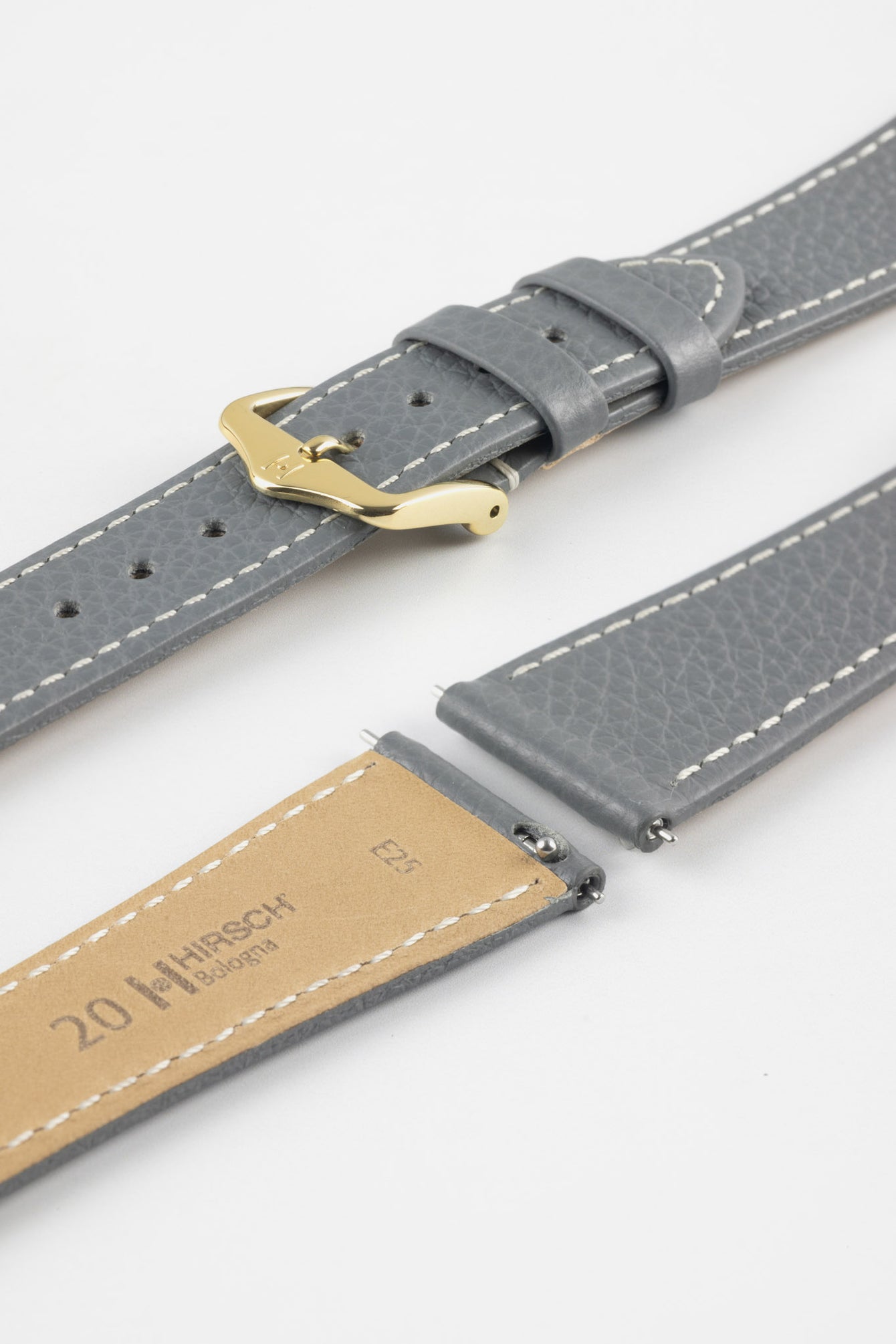 Close-up product image of a grey textured leather watch strap with white contrast stitching, displayed against a white background, featuring a polished gold-tone pin buckle and two keepers, alongside separate strap sections with exposed spring bars and a beige underside stamped with partial text “20 HIRSCH Bologna.”