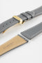 Close-up product image of a grey textured leather watch strap with white contrast stitching, displayed against a white background, featuring a polished gold-tone folding clasp and two keepers, alongside separate strap sections with exposed spring bars and a beige underside stamped with partial text “20 HIRSCH Bologna.”