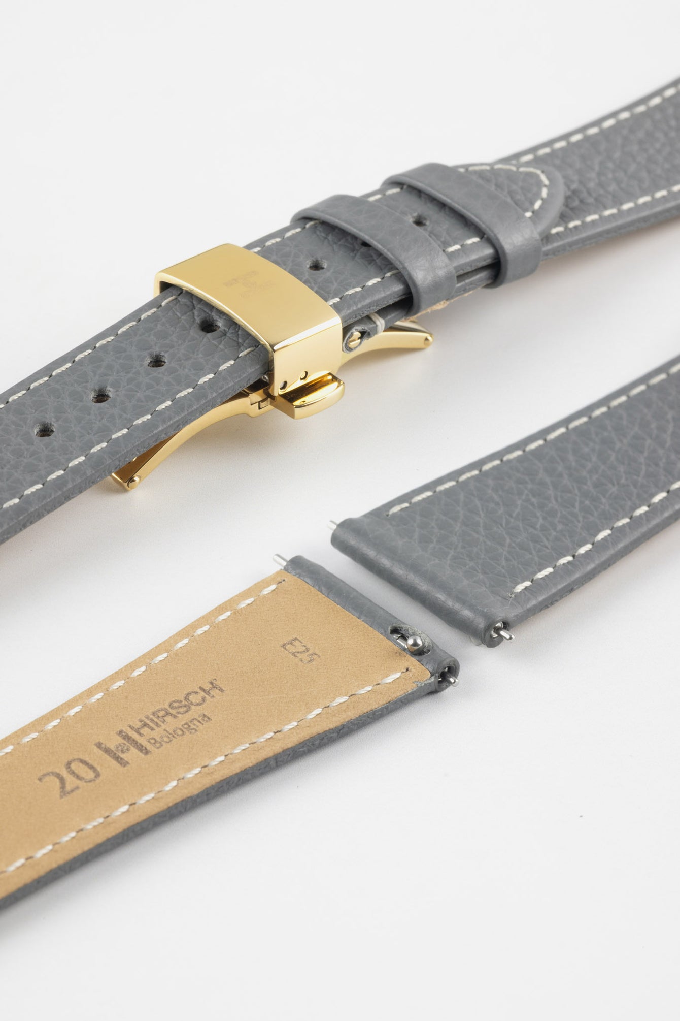 Grey leather watch strap with white stitching and a gold-tone deployment clasp, alongside extra strap pieces and a tan underside marked “HIRSCH Bologna” and “20.”