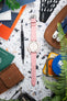 Top-down view of a pink chronograph wristwatch with a white dial and subdials, laid flat on a speckled surface and paired with a pink leather strap with white stitching. The watch is surrounded by everyday items including a brown leather wallet, a precision screwdriver, strap measuring tools labeled “Watch Obsession,” colorful cards, a tin container, and partially visible green plant leaves.