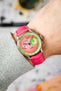 An overhead shot of a wrist adorned with a Studio Underd0g Bicompax Chronograph Watermelon watch, featuring a silver-toned case, a two-tone pink and green dial with sub-dials, and a vibrant hot pink Hirsch Duke leather strap with crocodile-style texture. The cuff of a light grey knit sweater is visible on the arm, and the background is blurred.