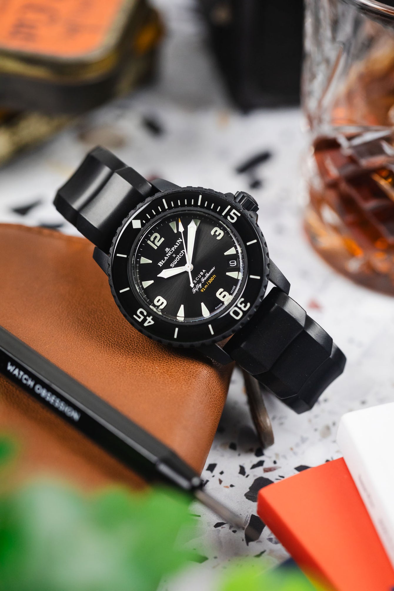 A Hirsch Extreme Rubber Diving watch strap fitted to a black blangpain dive watch leaning against a leather watch case.