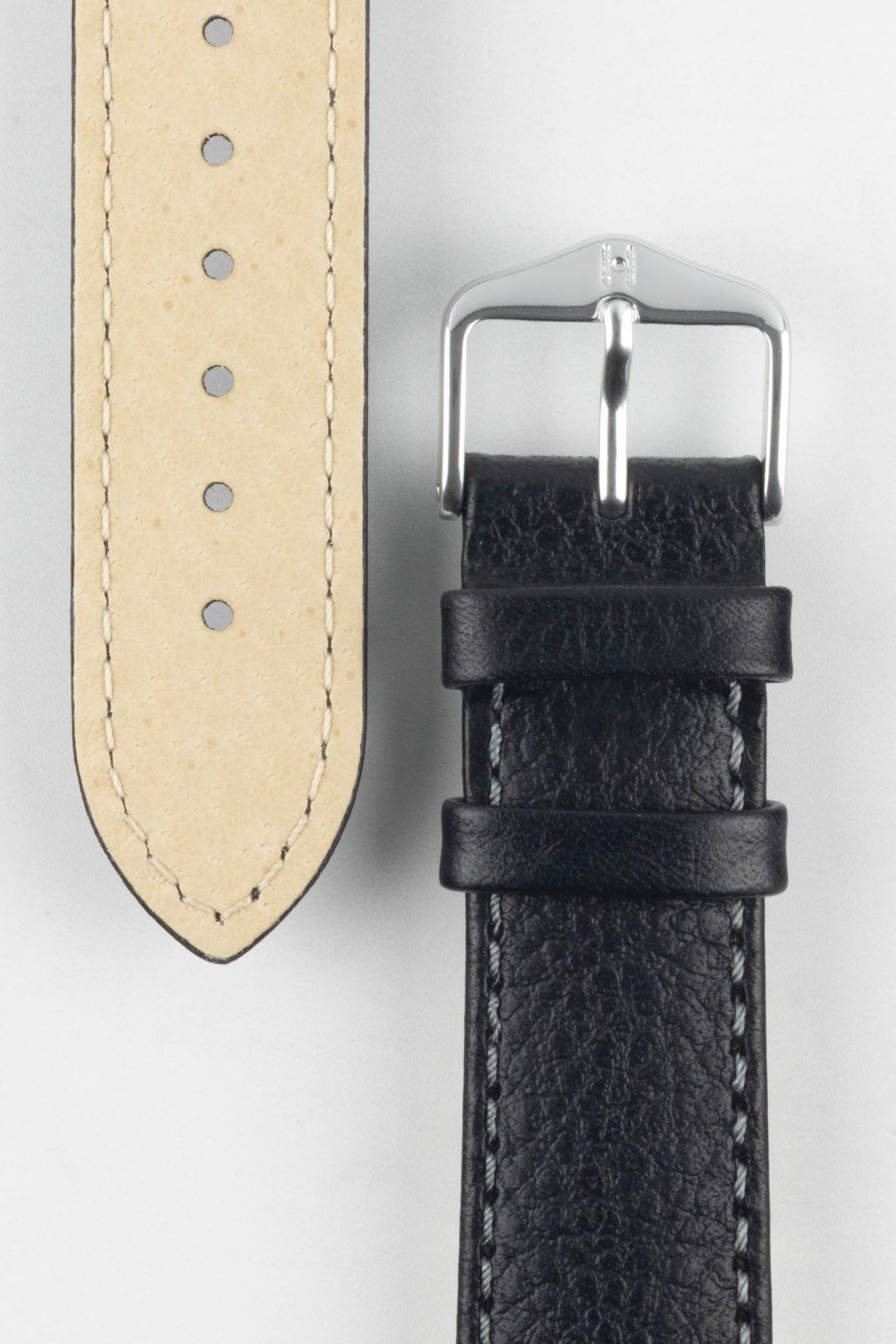 Close-up of a black watch strap showcasing its beige lining, grain texture, and classic silver buckle with a signature logo.