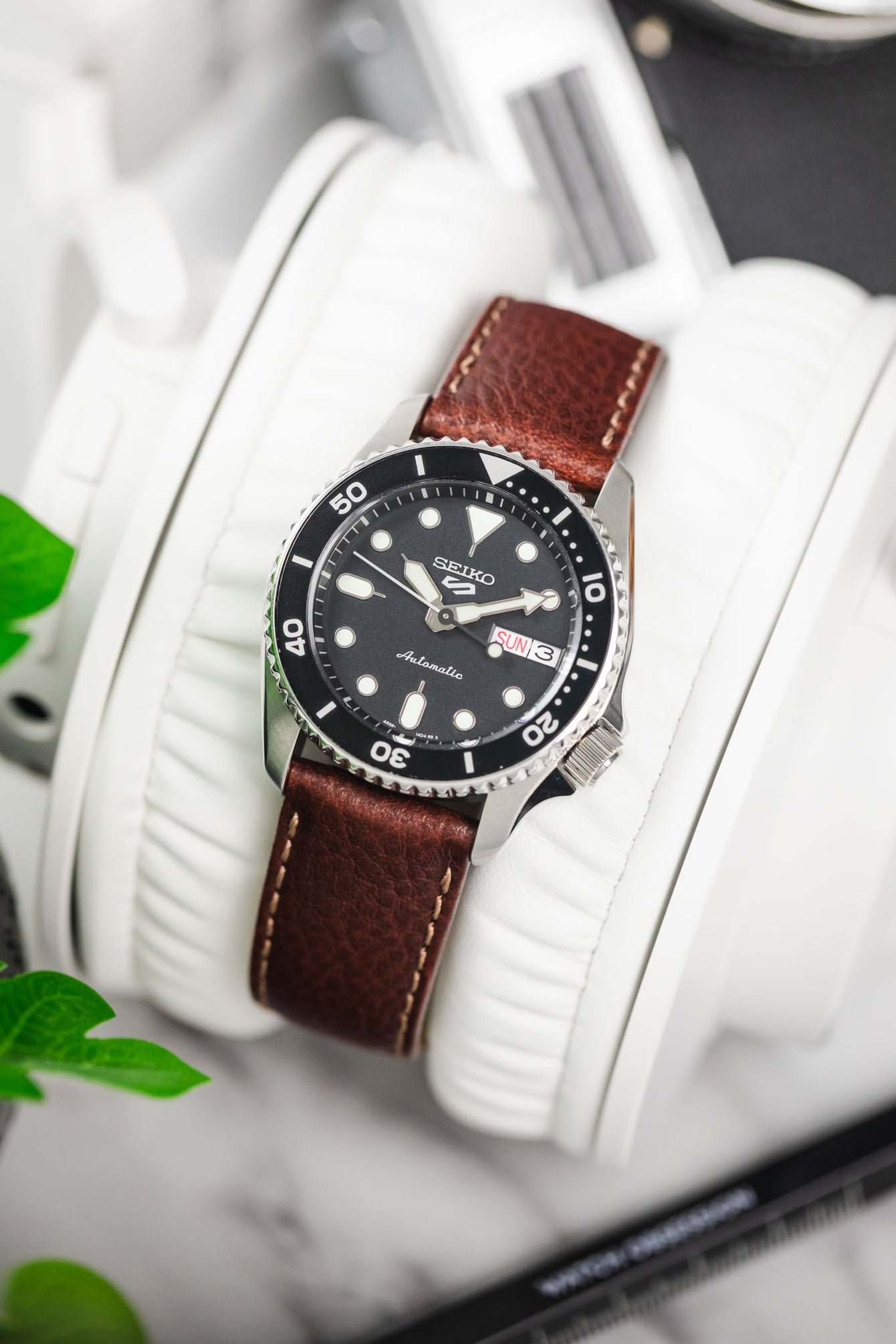 Seiko 5 Sports automatic diver on a brown leather watch strap with contrast stitching, resting on white headphones.