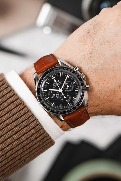 Black Omega Speedmaster Moonwatch fitted with Hirsch London alligator gold brown leather watch strap worn on wrist