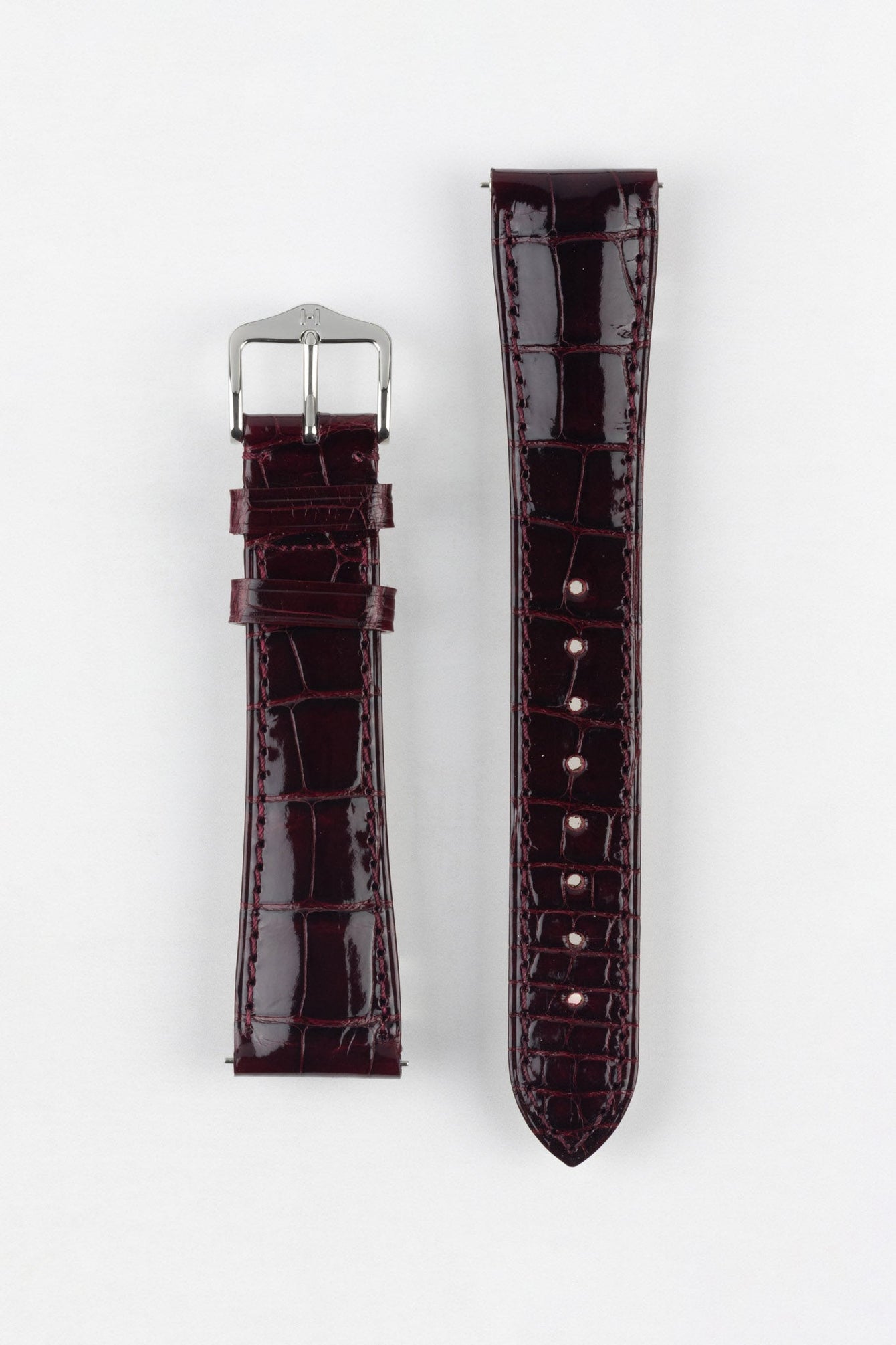 Product shot of a glossy burgundy crocodile-pattern leather watch strap displayed flat against a white background, showing both halves separately: one side with a polished silver-tone pin buckle and two keepers, and the other with multiple adjustment holes, highlighting the rich shine, textured grain, and matching stitching throughout.