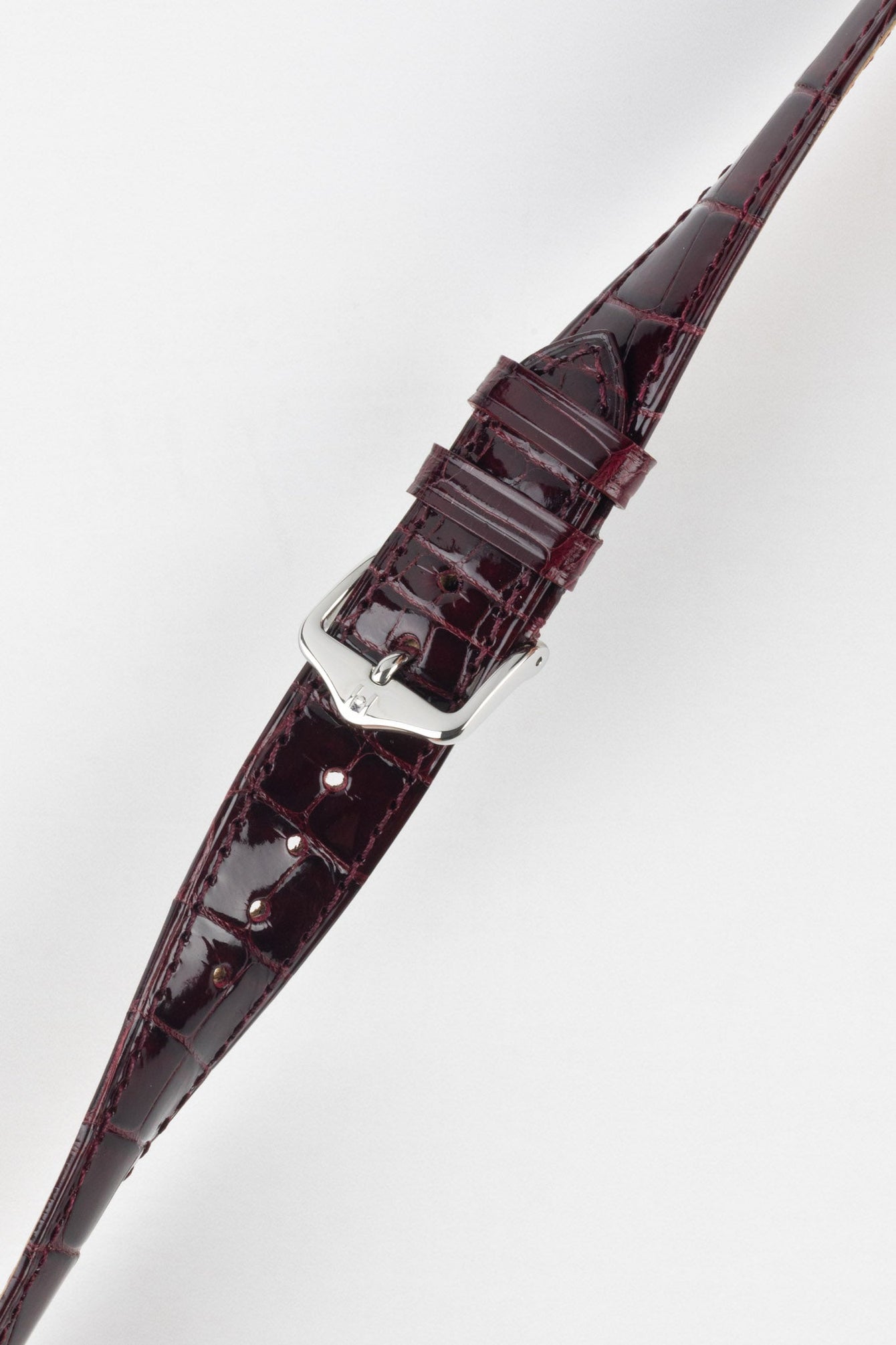 Close-up product image of a glossy burgundy crocodile-pattern leather watch strap with matching stitching, featuring a polished silver-tone pin buckle and two keepers, displayed against a clean white background with adjustment holes visible along the strap.