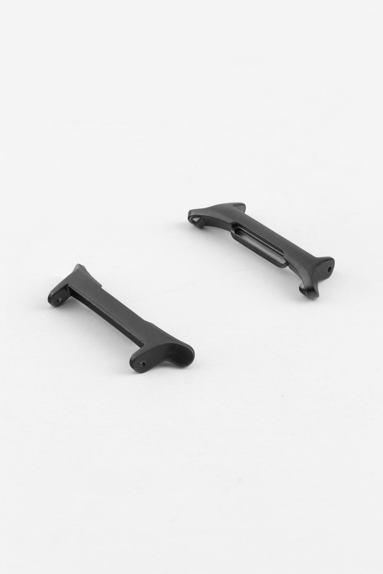 Two black adapter pieces for a watch strap, shown separated on a light grey background. Each piece features a matte finish with integrated fitting ends and a central recess for the strap attachment, highlighting their shape and construction for connecting straps to a compatible smartwatch.