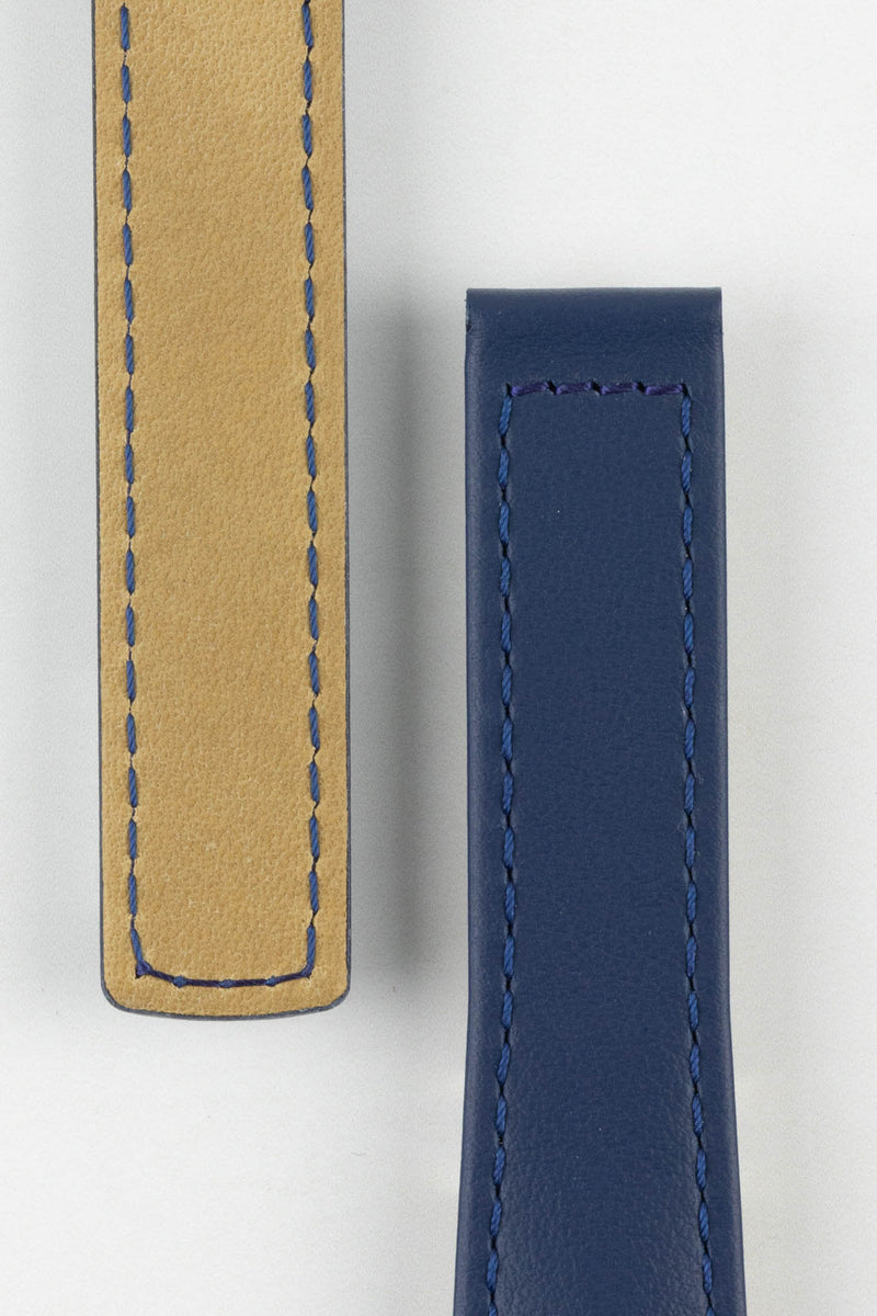 Close-up of a blue calf leather watch strap showing the front and beige underside on a light gray background. The strap features a smooth blue leather finish, matching blue stitching, and padded construction, highlighting the quality materials and craftsmanship.