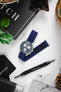 Flat lay of OMEGA x Swatch Mission on Earth watch on a blue textile strap with various watch accessories.