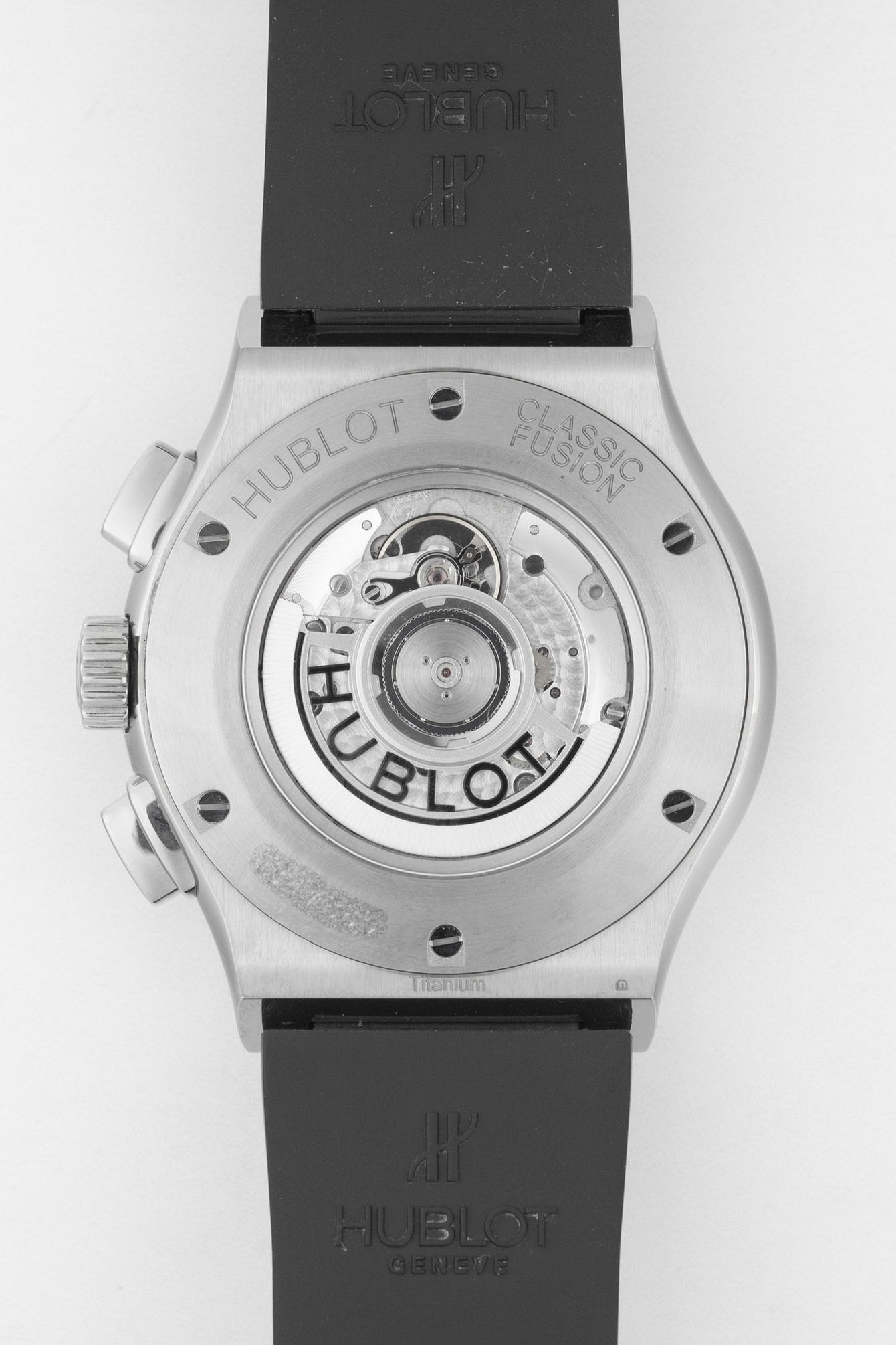 Close-up of the back of a Hublot Classic Fusion chronograph, showing the transparent caseback and automatic movement, with engraved “Hublot” and “Classic Fusion” on the titanium case and a black rubber strap.