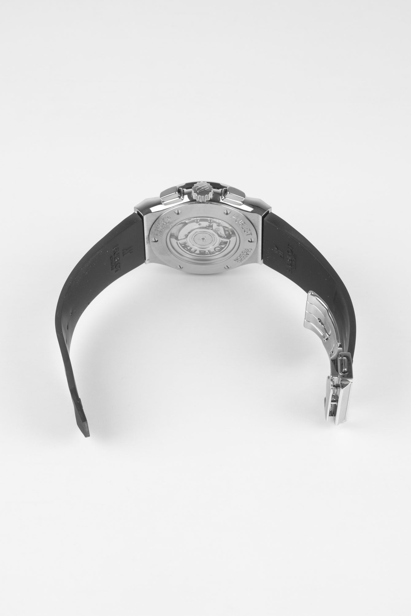 Back of a Hublot Classic Fusion chronograph watch on a black rubber strap, showing a transparent caseback and partially open deployment clasp against a white background.