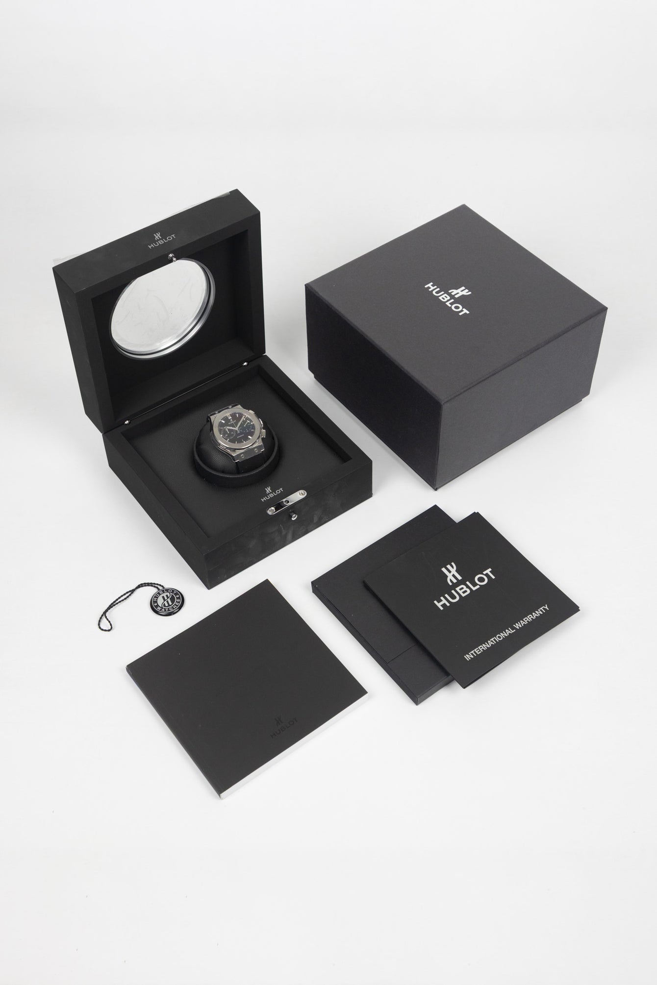 Studio shot of a Hublot Classic Fusion chronograph presented in its open black display box with branded packaging, warranty booklet, and accessories arranged on a white background.