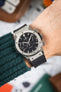Close-up of a Hublot Classic Fusion chronograph with a black dial and rubber strap, worn on a wrist with a green knit sleeve visible.