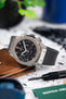Close-up of a Hublot Classic Fusion chronograph with a black dial and rubber strap, resting on a leather pouch beside a watch tool on a speckled surface.