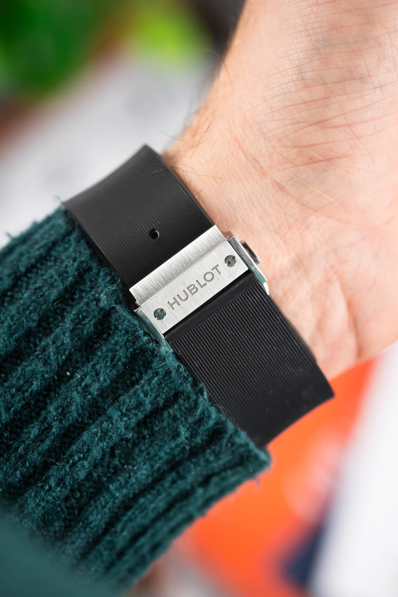 Close-up of a Hublot rubber strap on a wrist, featuring a brushed metal clasp engraved with “Hublot” and fine ridged texture on the strap.