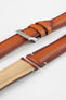 Angled close-up of a warm brown leather watch strap displayed on a light grey background, with multiple strap sections arranged side by side. One section features a polished silver tang buckle with an engraved logo and two matching leather keepers, while the others show the smooth, slightly burnished leather exterior and the tan suede underside near the lugs. The strap includes evenly spaced adjustment holes and subtle contrast stitching, highlighting the craftsmanship and construction.
