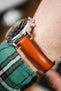 Close-up of a brown leather watch strap with a smooth finish and light stitching, worn on a wrist, highlighting the polished steel case and side profile.