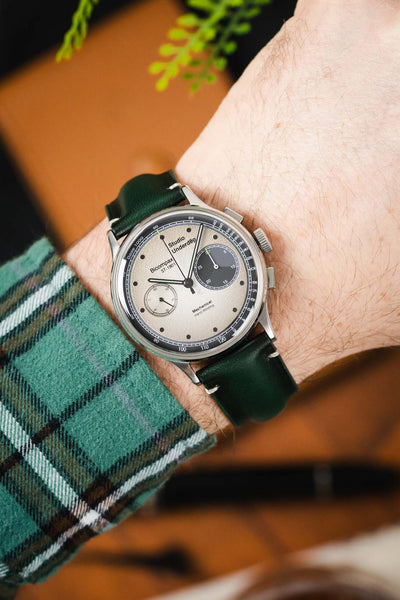 Close-up of a Studio Underd0g Bicompax watch with a textured silver dial and dark green leather strap, worn on a wrist.
