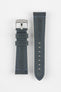 Two blue-grey leather watch strap pieces displayed vertically on a light grey background, featuring a matte, finely textured finish with contrast light blue stitching along the edges. One strap section includes a brushed silver tang buckle with an engraved logo and two leather keepers, while the other shows a tapered end with evenly spaced oval adjustment holes. The clean stitching and structured shape highlight the strap’s modern, durable design.