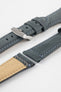 Blue-grey leather watch strap with light blue stitching on a grey background, shown in angled close-up with a brushed silver buckle, adjustment holes, and tan suede underside sections.