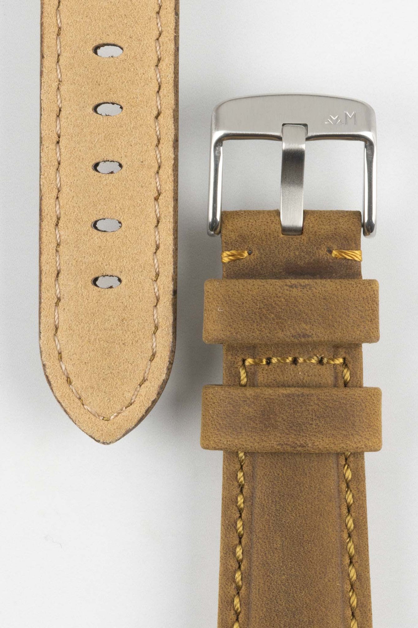 Close-up of a tan-brown leather watch strap with yellow stitching, showing a silver buckle, adjustment holes, and beige suede underside on a light grey background.