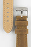 Close-up of a tan-brown leather watch strap with yellow stitching, showing a silver buckle, adjustment holes, and beige suede underside on a light grey background.