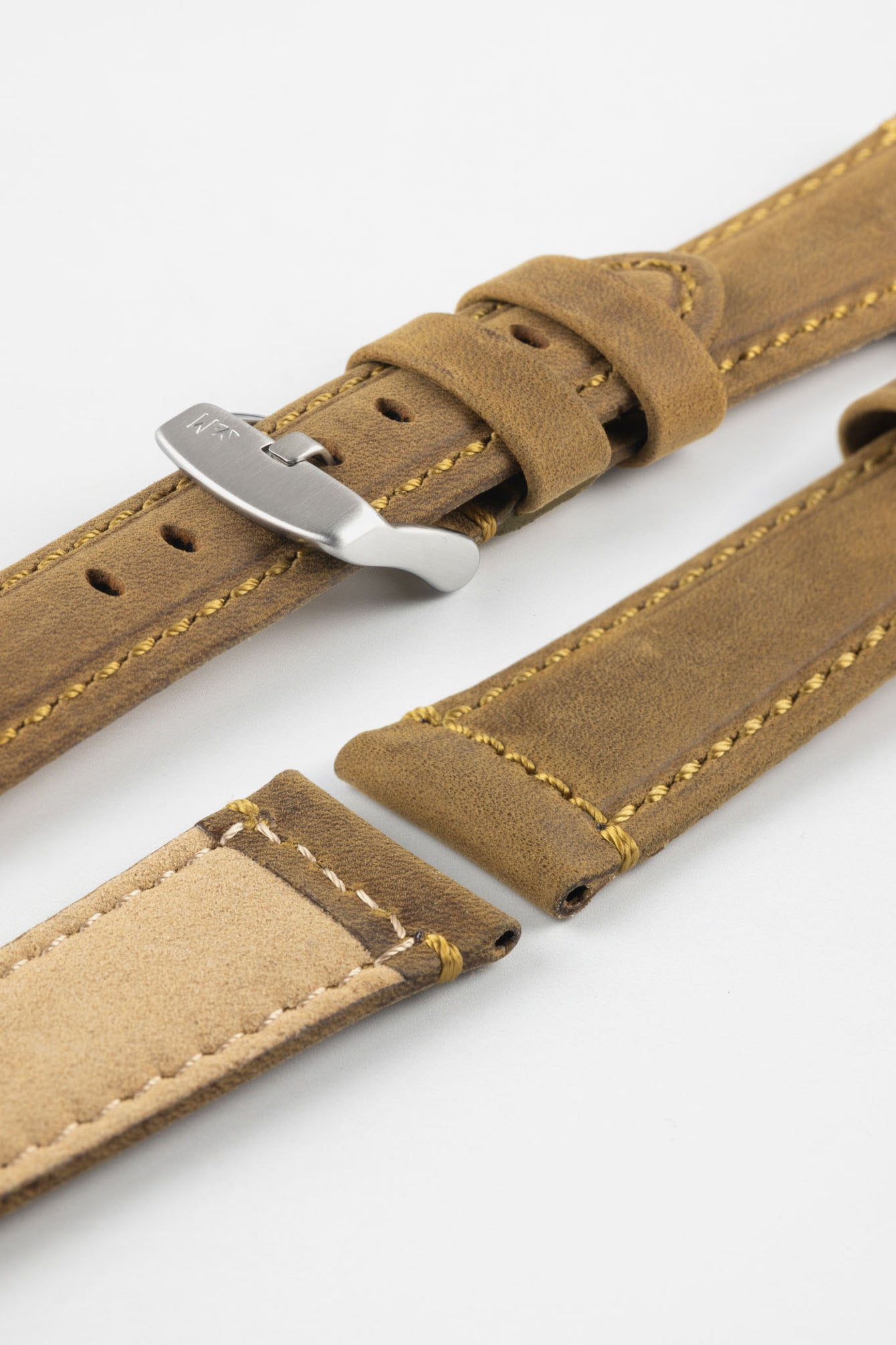 Tan-brown leather watch strap with yellow stitching, shown in angled close-up with a silver buckle, adjustment holes, and beige suede underside.
