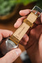 Close-up of the underside of a tan leather watch strap held in hand, showing stitching, keeper loop, and engraved text “Fatto a Mano” and “22/18,” attached to a steel caseback.