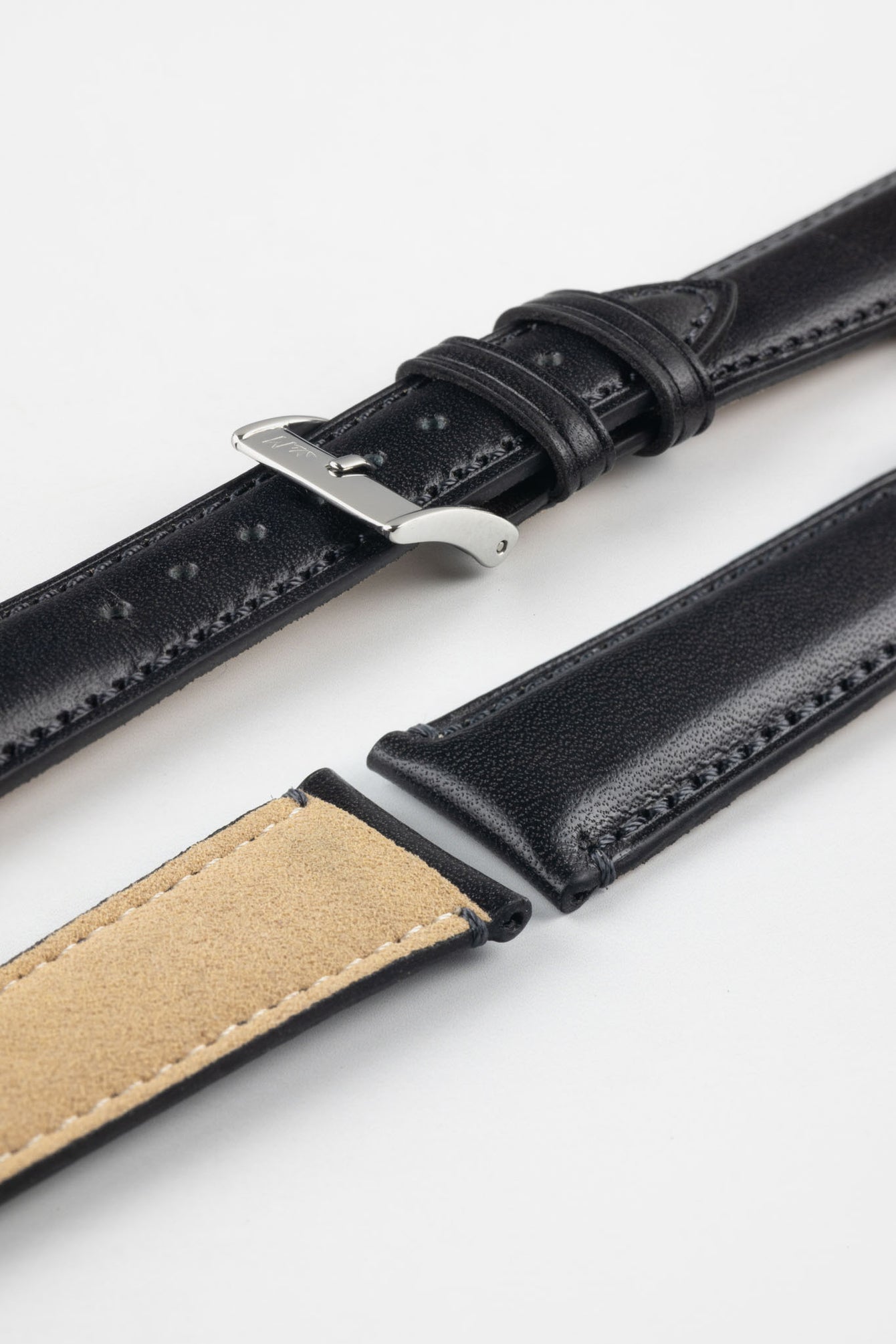 Black leather watch strap with black stitching, shown in angled close-up with a silver buckle, adjustment holes, and beige suede underside.