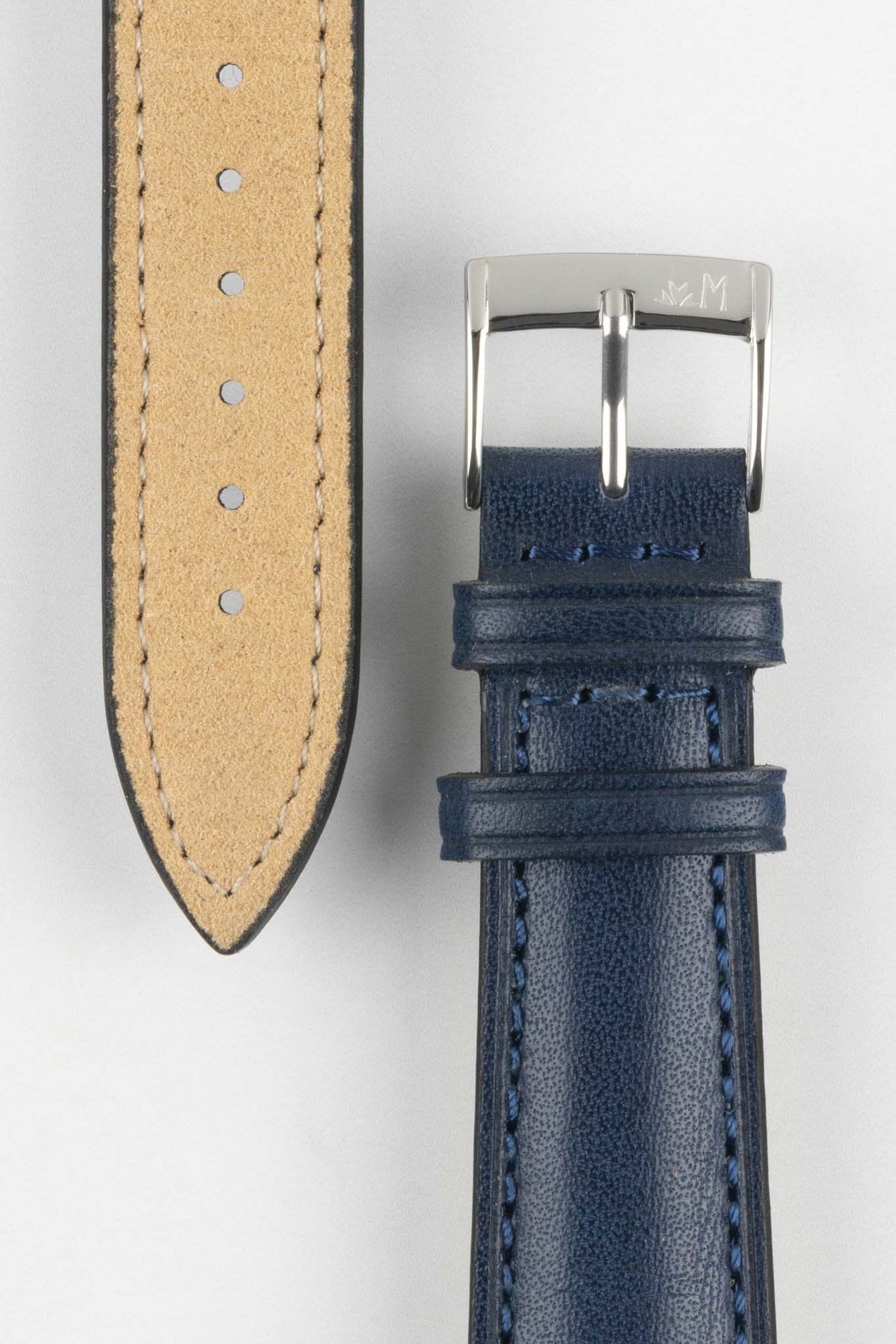 Close-up of a blue leather watch strap showing a silver buckle, adjustment holes, and beige suede underside on a light grey background.