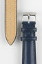 Close-up of a blue leather watch strap showing a silver buckle, adjustment holes, and beige suede underside on a light grey background.